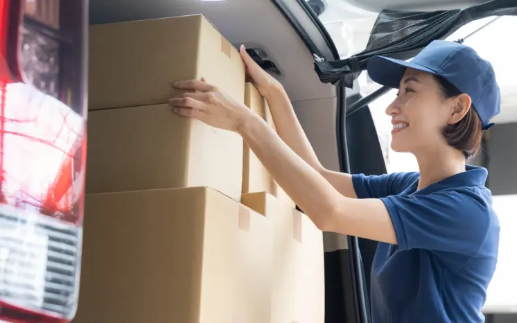 配送車のトランクに荷物を積み込む女性ドライバー